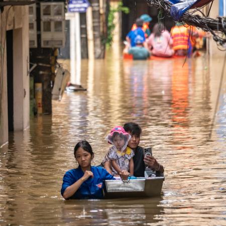  A woman, a man and child navigate a flooded street, showcasing the impact of heavy rainfall on their surroundings.