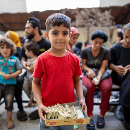 A boy in red shirt stands in front of people sitting together in Lebanon