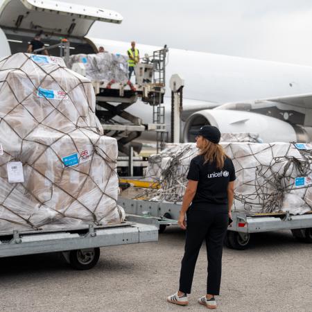 A UNICEF worker oversees humanitarian aid being offloaded from a cargo airplane.