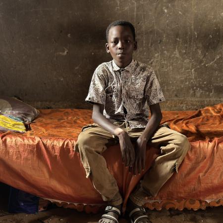 A boy sits in his home as he looks towards the camera in Sudan