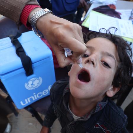 A child is being vaccinated while UNICEF's vaccination cold storage can been seen as well