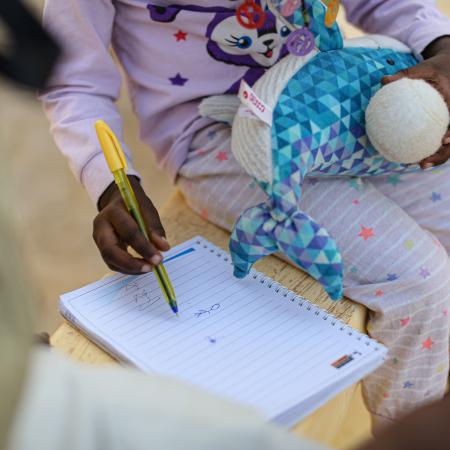 Assourita*, a 5-year-old girl scribbles on a notepad. 