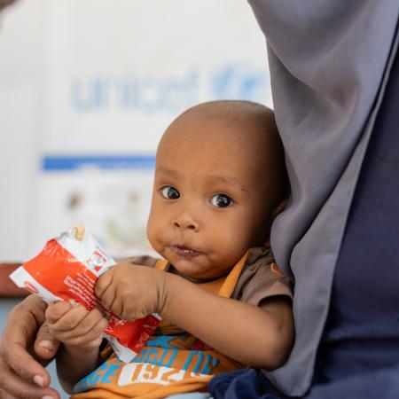 A child sits in their mother's lap as they hold a packet of RUTF in Sudan