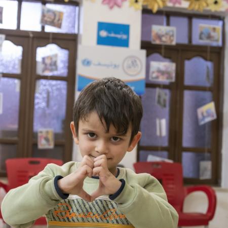 A child makes heart shape with their hands at a child protection centre in Syria 