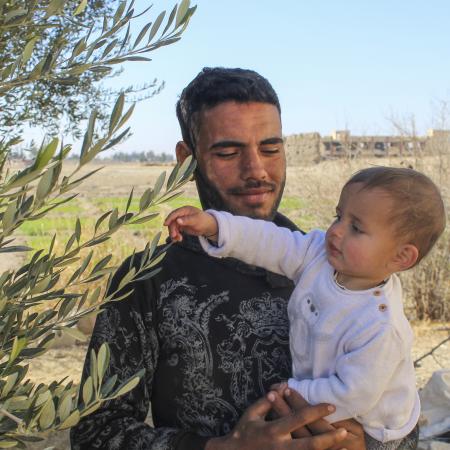 Mohamed, Morei’s father, holds his one-year-old son in the yard of their home in Obada village, Rural Damascus, Syria.