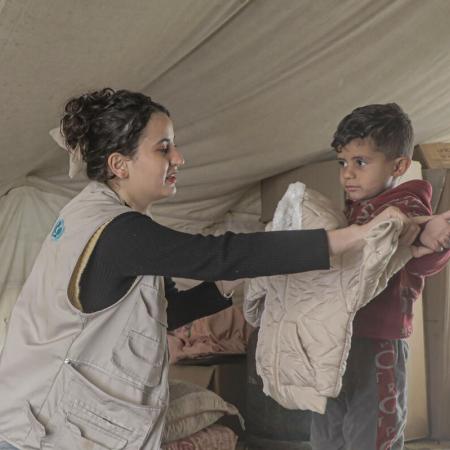 UNICEF staff member helps a young child unpack winter clothing distributed for children aged 3 to 5 years old in central Gaza in the State of Palestine.