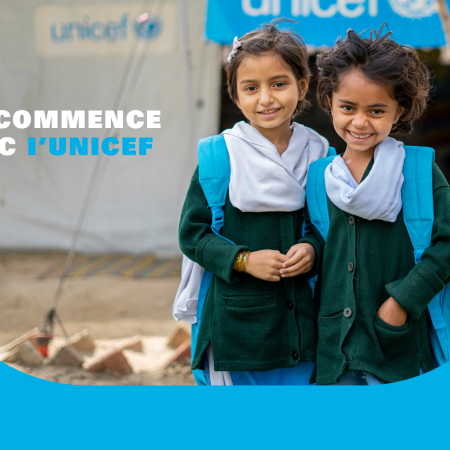 Deux jeunes filles portant des sacs à dos bleus de l’UNICEF devant un centre d’apprentissage temporaire financé par l’organisme sourient à l’objectif.