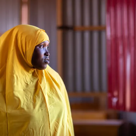 A girl wearing a yellow uniform with a yellow scarf stands by a door looking outside contemplatively.
