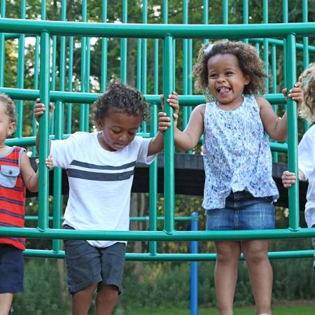 Four young children play outdoors on a play structure. 