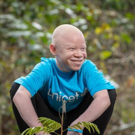 Emmanuel, a young climate advocate, plants a tree while wearing a blue UNICEF t-shirt.